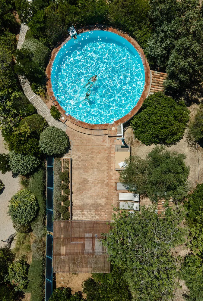 Looking straight down on a round pool among the trees in Portugal, a swimmer in the water