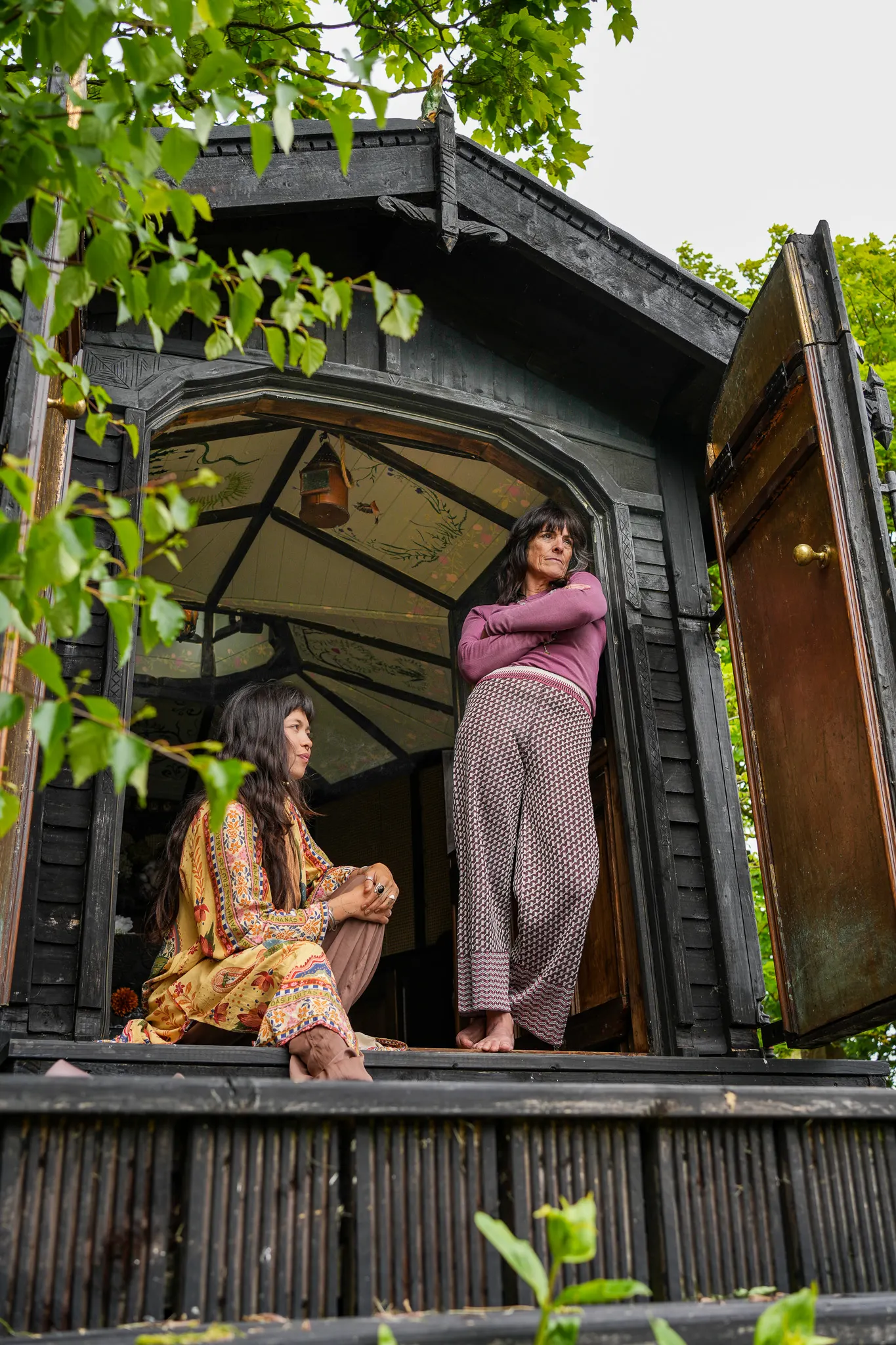 Catherine standing in the doorway of an ornate wooden summer house, with Dani sitting on the step