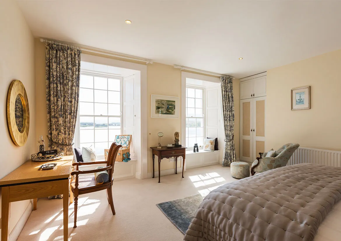 A bright guest bedroom with tall sash windows looking out to the bay