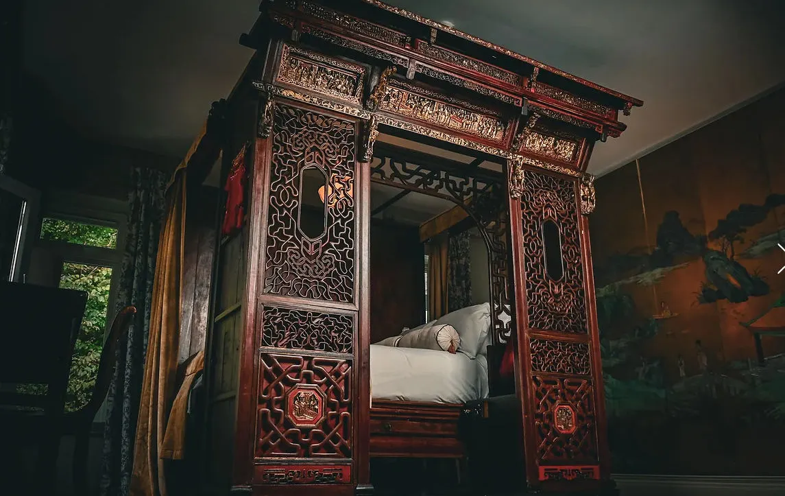 An ornately carved antique four-poster bed in a dark, richly decorated room