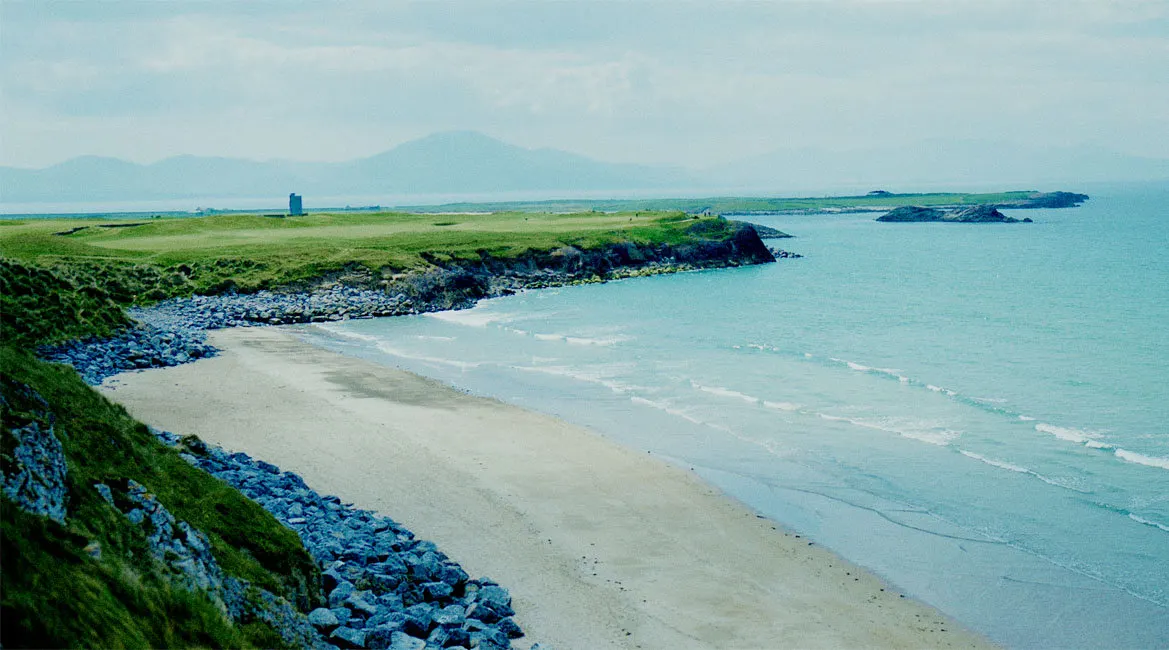 A curve of quiet beach below green links on the Kerry coast