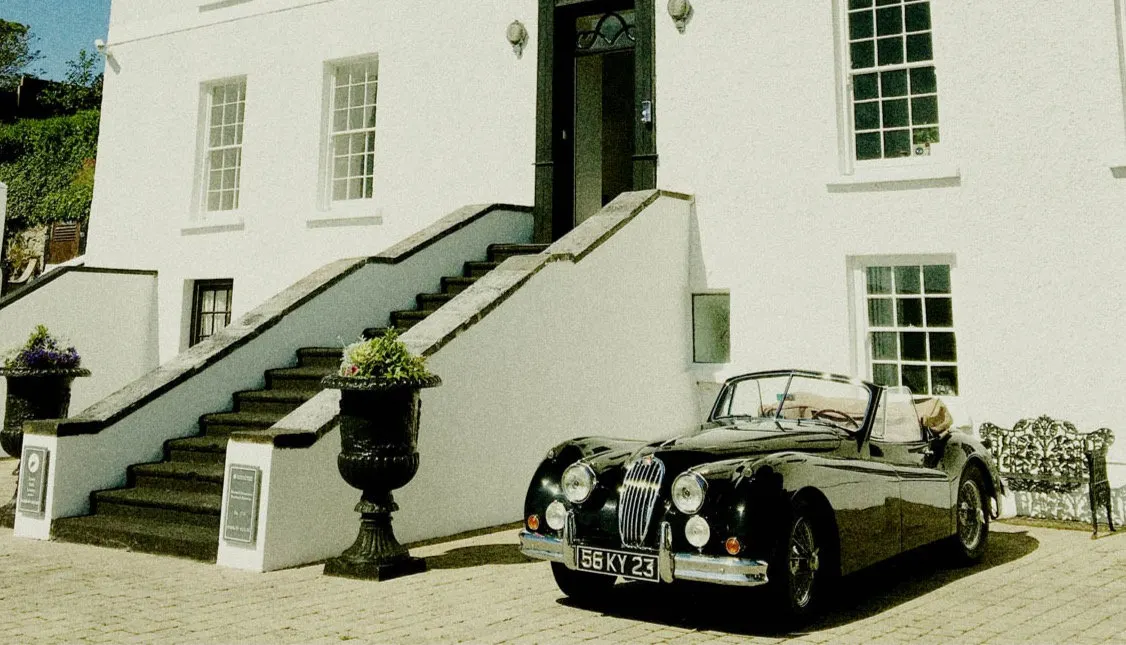 The white front of Barrow House with a vintage car at the steps