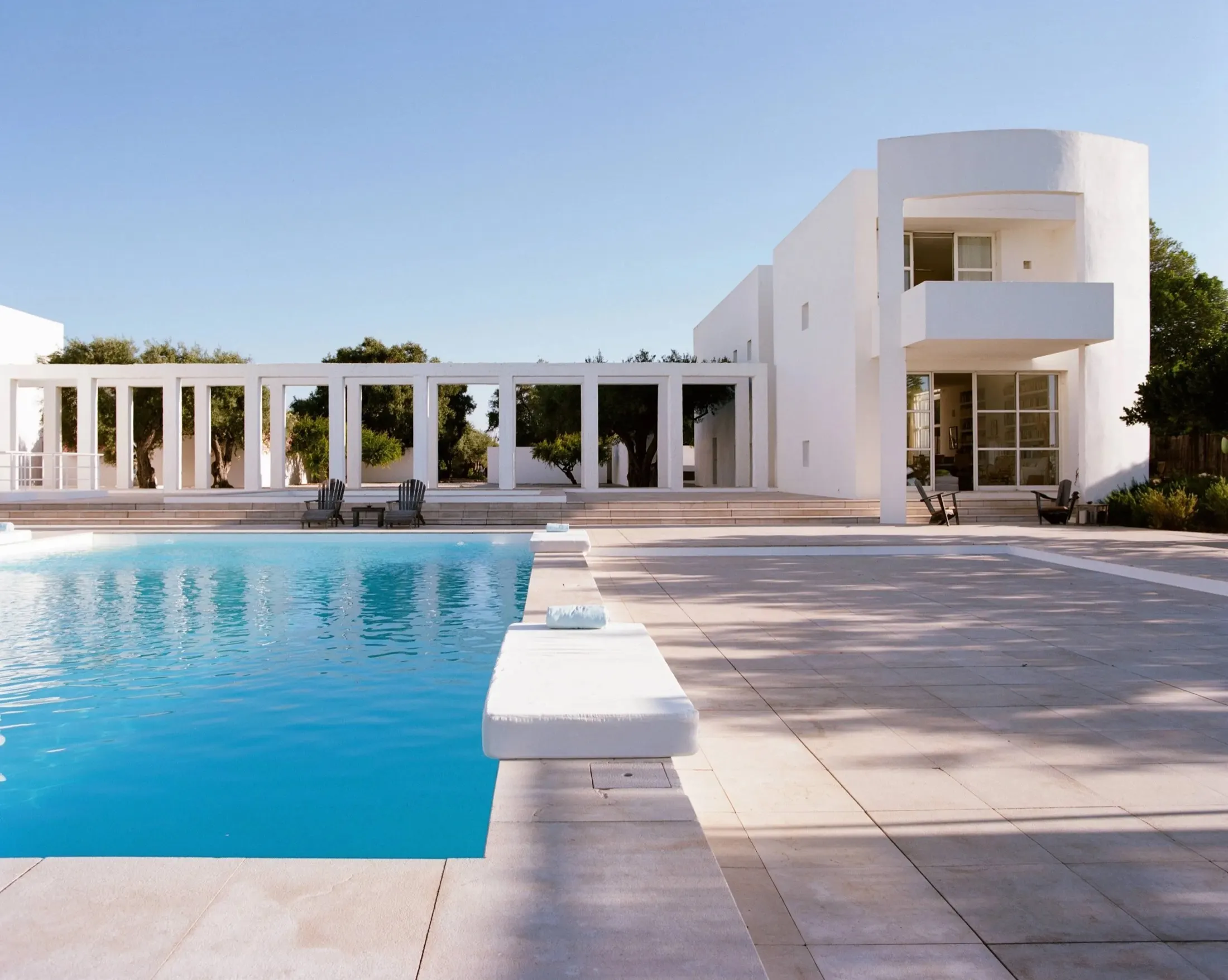 The pool, colonnade and white house at Quinta do Muro under a clear blue sky