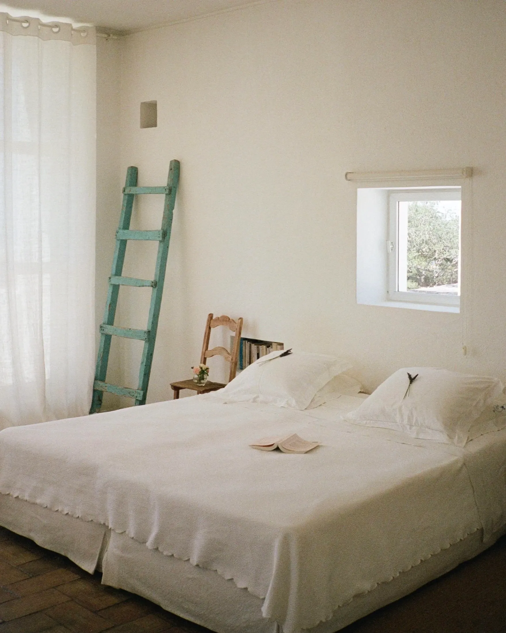 A calm white bedroom with twin beds side by side and a blue-green ladder shelf
