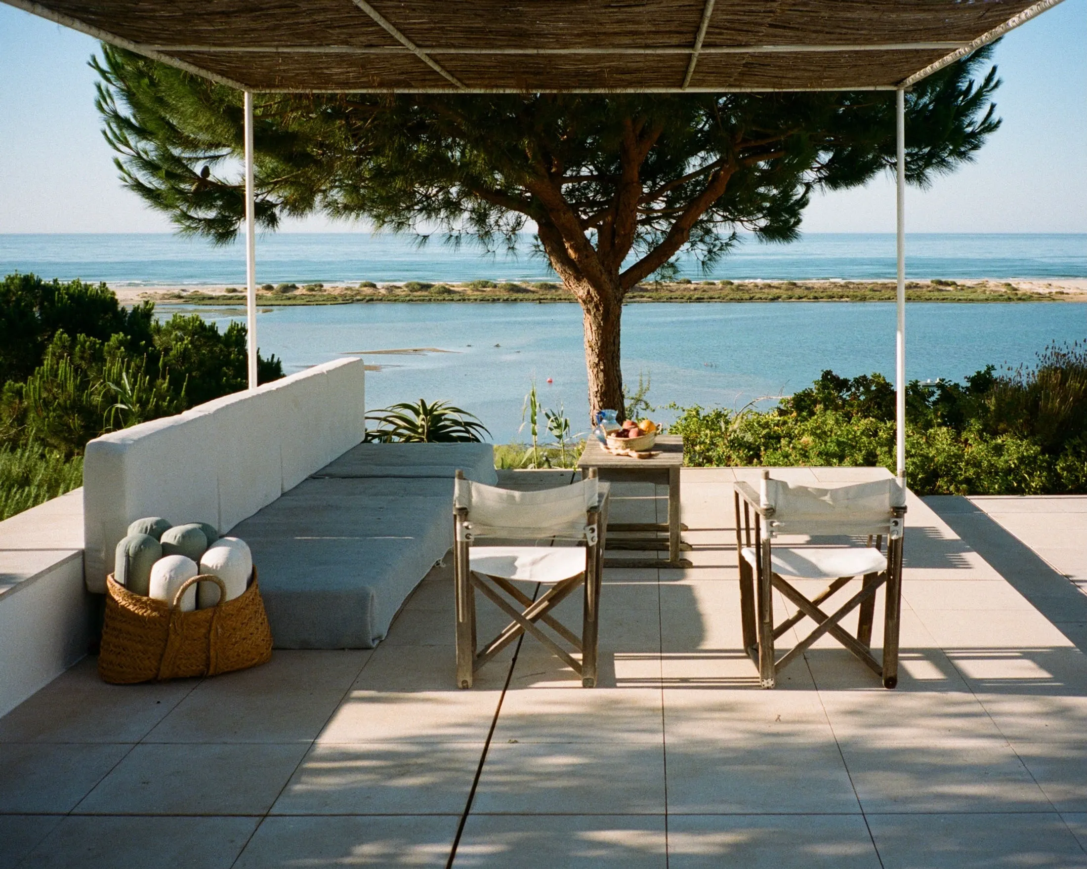 A shaded terrace with two canvas chairs under a pine, looking out over the Ria Formosa lagoon